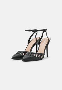 Sapatos de salto alto pretos com biqueira pontuda, design de parte superior recortada e tira no tornozelo. Apresentam um salto agulha e uma textura de pele suave.