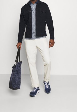 Dark denim jacket, gray polo, cream trousers, and navy sneakers. Holding a navy bag with a shoulder strap. Casual outfit.