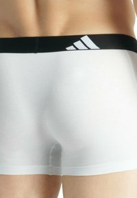 Vita bomullboxer med svart elastisk midjeband som har tre vita diagonala ränder. Slät textur och åtsittande design.