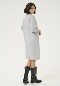 Robe en tricot gris avec des manches trois-quarts, coupe à genoux, poches latérales, assortie à des bottes noires brillantes mi-mollet avec des boucles.
