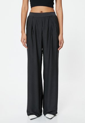 Pantalones de pierna ancha negros con patrón de lunares blancos, hechos de una tela ligera. Cuentan con un frente plisado y una cinturilla elástica.