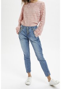 Pink lace long-sleeve top with floral patterns and scalloped hem, paired with light blue denim jeans featuring metal button accents and side pockets.