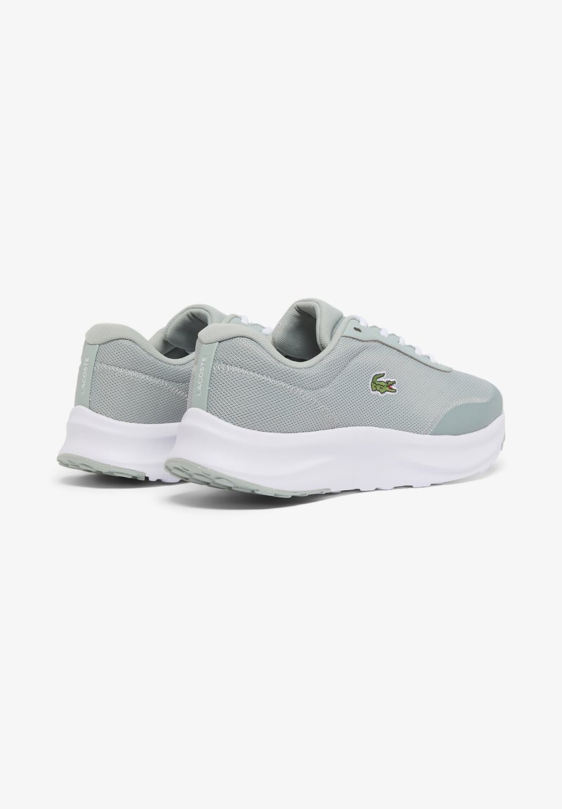 Baskets Lacoste gris clair avec semelles blanches, logo crocodile vert sur les côtés et texture en tissu mesh, présentées vues de l'arrière et de côté.
