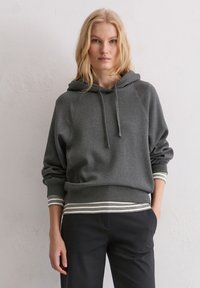 Felpa grigia con cappuccio e vestibilità comoda, con polsini e orlo a coste caratterizzati da strisce bianche. Tessuto morbido con una superficie liscia. Pantaloni neri.