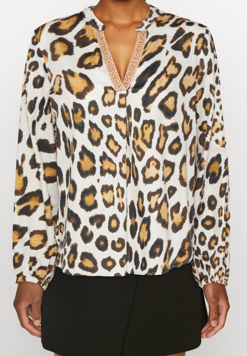 Blusa a maniche lunghe con stampa leopardata in bianco, marrone e nero. Presenta una scollatura a V con dettagli ricamati e polsini elasticizzati.