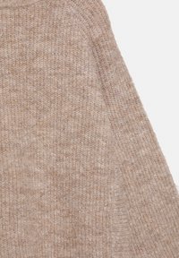 Béžový pletený sveter s textúrovaným povrchom. Tkanina je mäkká s voľným tkaním, s výrazným rebrovaným zdobením pozdĺž okrajov.