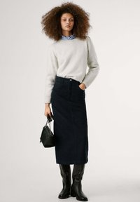 Helles graues Strickpullover, dunkelblauer Jeansrock, schwarze knielange Stiefel, hält eine kleine schwarze Handtasche mit einer Kettenriemen, nahtloses Design.