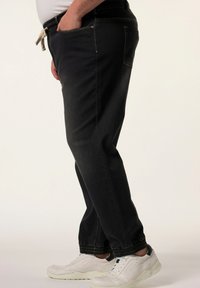 Mustat farkkutrikoot joustavalla vyötäröllä, sivutaskuilla ja valkoisilla ompeluyksityiskohdilla, yhdistettynä valkoisiin matalavarpaisiin tennareihin.