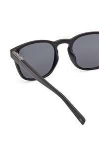 Czarne okulary przeciwsłoneczne o matowym wykończeniu, kanciastym szkielecie, ciemnych soczewkach i prostych ramionach z delikatnym logo po boku.