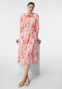 Koronkowa sukienka w kwiatowy wzór w kolorze białym, z zapięciem na guziki z przodu, rękawy do łokci, talia podkreślona paskiem, długość do kolan, zestawiona z białymi sandałami na paski.