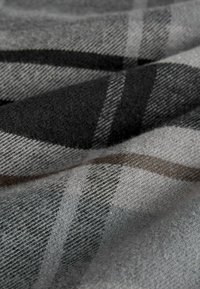 Szary materiał w kratę o miękkiej fakturze przypominającej wełnę. Wzory obejmują czarne i jasnoszare pasy z delikatnymi brązowymi akcentami.