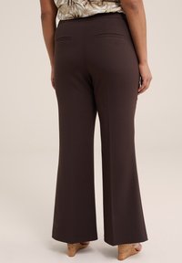 Pantalones acampanados marrones con una tela suave y dos bolsillos traseros, combinados con zapatos de un color claro. El diseño presenta una cintura alta.