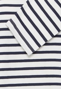 Chemise en coton rayée bleu marine et blanche à manches longues, avec un ourlet cousu et une texture douce et lisse. Les rayures sont espacées uniformément.