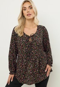 Schwarze Blumenbluse mit langen Ärmeln, einem Bindeband am Ausschnitt und einem Peplum-Saum. Verfügt über kleine, bunte Blumen und einen leichten Stoff.