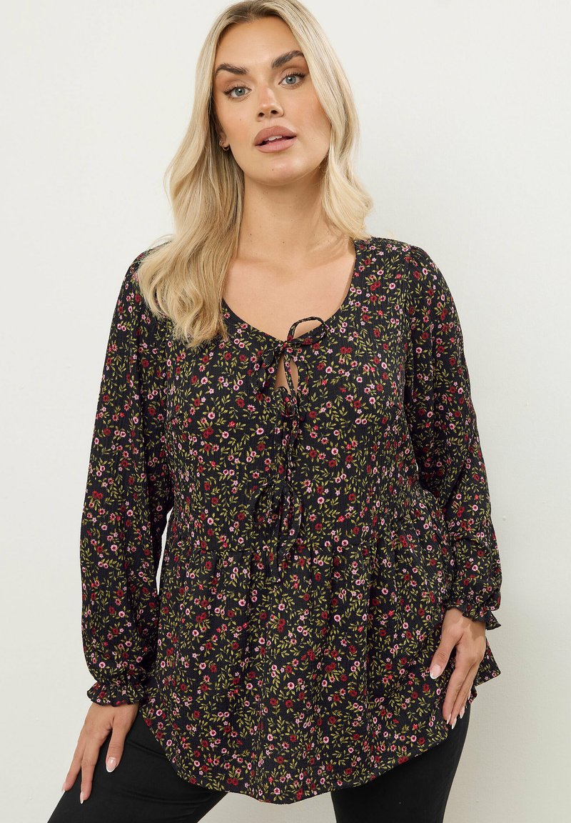 Schwarze Blumenbluse mit langen Ärmeln, einem Bindeband am Ausschnitt und einem Peplum-Saum. Verfügt über kleine, bunte Blumen und einen leichten Stoff.