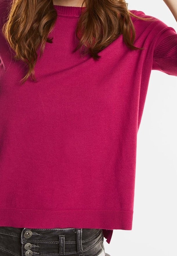 Fuchsia stickad tröja med korta ärmar, med rund halsringning och ribbad nederkant, tillsammans med högmidjade mörka jeans med knappar.