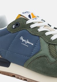 Sapatilha verde e azul com materiais mistos, apresentando camurça, rede e sintético. Cadarços brancos, sola castanha e detalhe do logótipo.