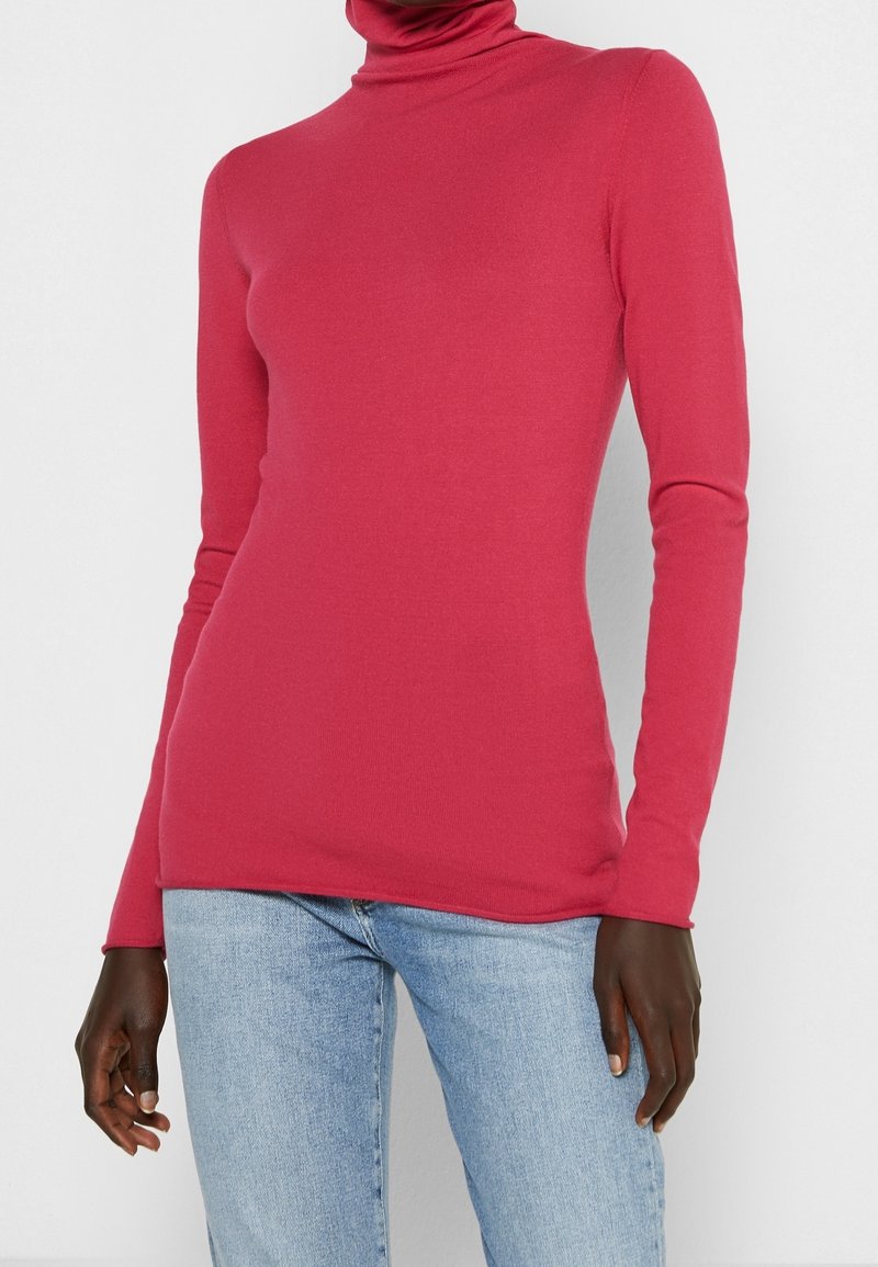 Aansluitende coltrui in helder roze, gemaakt van een gladde, rekbare stof met lange mouwen en een geribbelde halslijn. Gecombineerd met lichtblauwe jeans.