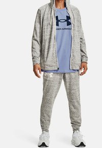 Felpa grigia mélange con zip sopra una t-shirt azzurra chiara con un logo nero, abbinata a pantaloni gray mélange e scarpe sportive bianche.