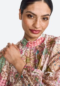 Blusa de tejido ligero con estampado floral, que cuenta con un cuello alto, mangas abullonadas y puños elastizados con acentos coloridos.