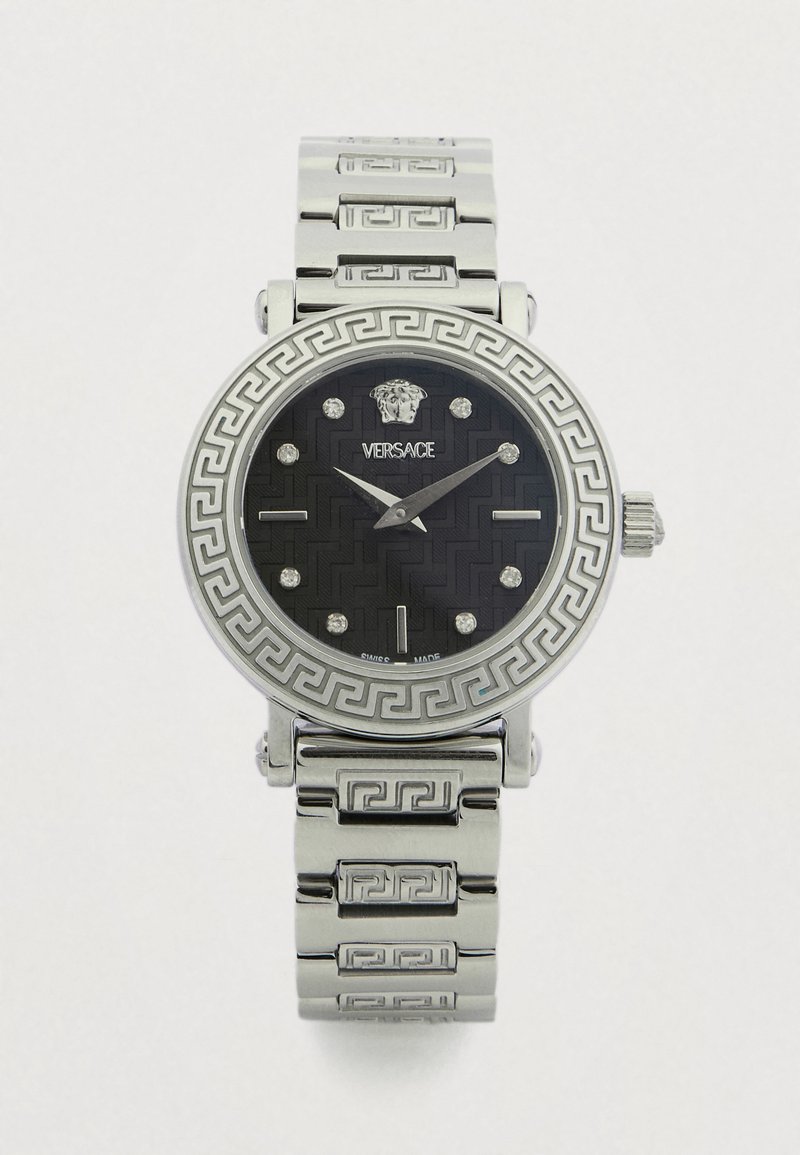 Rozsdamentes acél óra kerek, fekete mintás számlappal, ezüst órajelzésekkel és görög kulcs mintás lünettával. Tartalmazza a Versace logót és ezüst színű karkötőt.