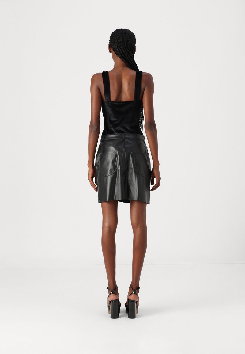 Minifalda de imitación cuero negra con cinturilla alta, bolsillos traseros y una textura suave. Combinada con una camiseta sin mangas negra y tacones gruesos.