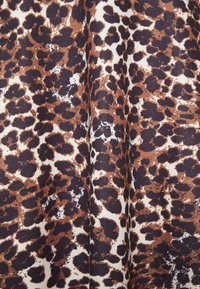 Tecido com padrão de leopardo apresentando uma superfície texturizada em castanho e preto sobre um fundo creme, exibindo vários tamanhos e arranjos de manchas.
