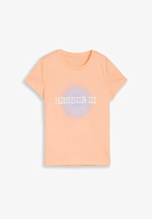 Perzikkleurig T-shirt met korte mouwen, een ronde hals en de tekst "BREATH IN" over een subtiele blauwe cirkelvormige verloop aan de voorkant.