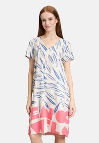 Leinenkleid mit V-Ausschnitt und kurzen Ärmeln, das blaue Fischmuster auf einem beigen Hintergrund und fetten pinken Text am unteren Rand aufweist.