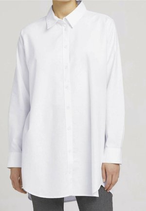 Biała koszula z długim rękawem zapinana na guziki, noszona na szarych spodniach, z klasycznym kołnierzem i zapinanymi mankietami, pokazana od szyi do bioder.