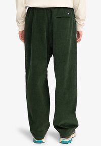 Grønne corduroy bukser med løs pasform, der har en baglomme og en tekstureret overflade. Taljen har et blødt elastisk bånd for komfort.