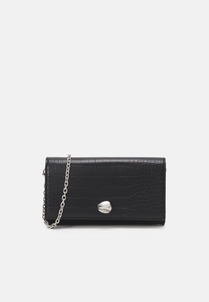 Pochette en cuir noir texturé avec bandoulière en chaîne argentée et fermoir ovale argenté, présentée sur un fond clair uni.