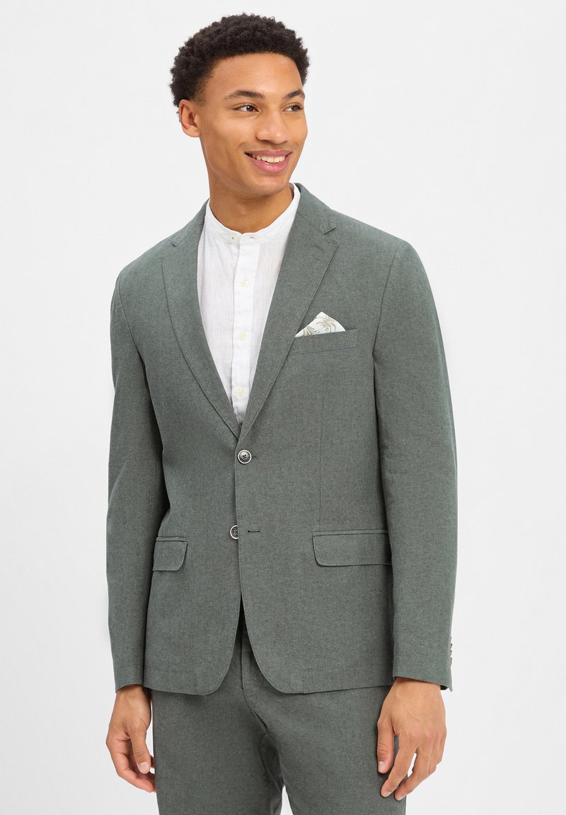 Grijze blazer met een gestructureerde afwerking, twee knopen en klepzakken. Draag het over een wit overhemd met kraag, met een patroon op de pochette.