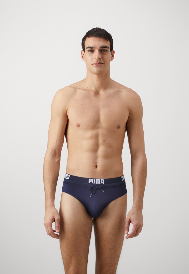 Tamno modre hlače z belim pasom, ki se kontrastno izstopa in nosi logo "PUMA". Gladka tekstura in prilegajoč dizajn.