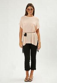 Hellrosa gestricktes Oberteil mit kurzen Ärmeln und lockerer Passform, kombiniert mit schwarzen cropped Hosen mit Spitzenabschluss und schwarzen Flip-Flops.