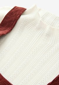 Strukturiertweißer Stoff mit vertikalen Rippungen und kleinen Perforationen, akzentuiert durch einen tiefroten, gerippten Kragen und Schultern.