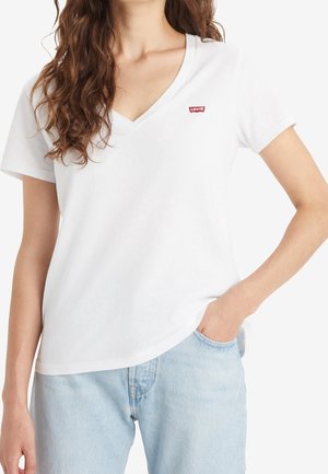 Kvinde iført en hvid Levi's t-shirt med V-hals og korte ærmer samt lyseblå jeans, den ene hånd i lommen.