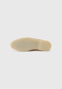 Sko såle med en gjennomsiktig beige gummibunn, glatt tekstur og buet form; har minimal merkevarebygging på siden.