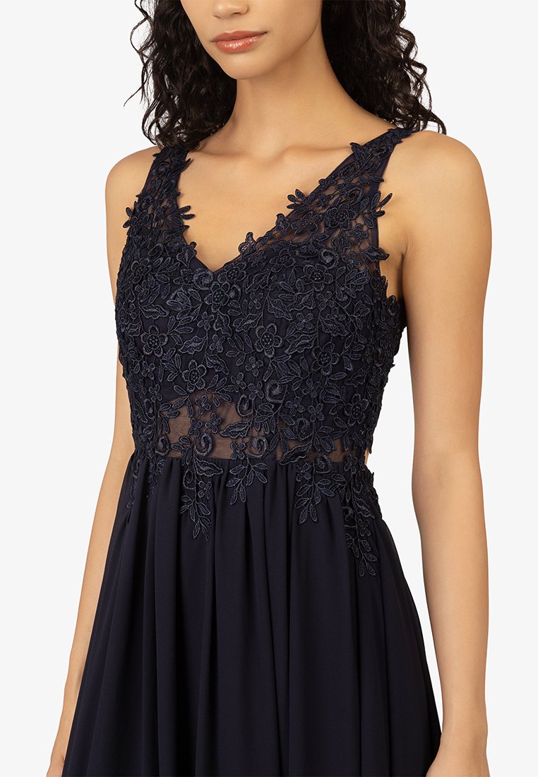 Granatowa sukienka z koronkowymi haftami w kwiaty na dekolcie w serek, z przezroczystymi panelami oraz zwiewną spódnicą z delikatnymi fałdami.