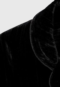 Tejido de terciopelo negro con una textura suave y un brillo sutil, que presenta un diseño de cuello redondeado y un patrón sutilmente ondulado.