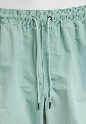 Pantaloni da bagno verde menta chiaro con vita elastica, cordino regolabile e texture liscia, leggermente lucida.