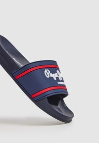 Námořnické gumové sandály na skluzu s červenými pruhy a bílým logem. Otevřený design na špičce, plochá podrážka, hladká textura, vhodné pro každodenní nošení.