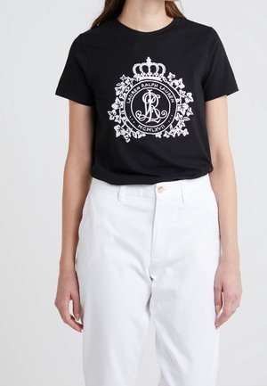 Schwarzes T-Shirt mit einem weißen Grafikdesign, das eine Krone und verzierte Schriftzüge zeigt, kombiniert mit hoch taillierten weißen Hosen.