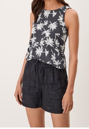 Ærmeløs sort top med hvidt palmeprint kombineret med sorte linnedshorts med snøre, båret af en stående person.