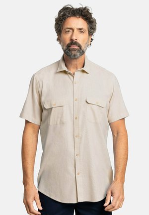 Camisa de manga corta color beige claro, con botones en la parte delantera, dos bolsillos en el pecho, textura suave y un sutil patrón horizontal. Diseño de cuello clásico.