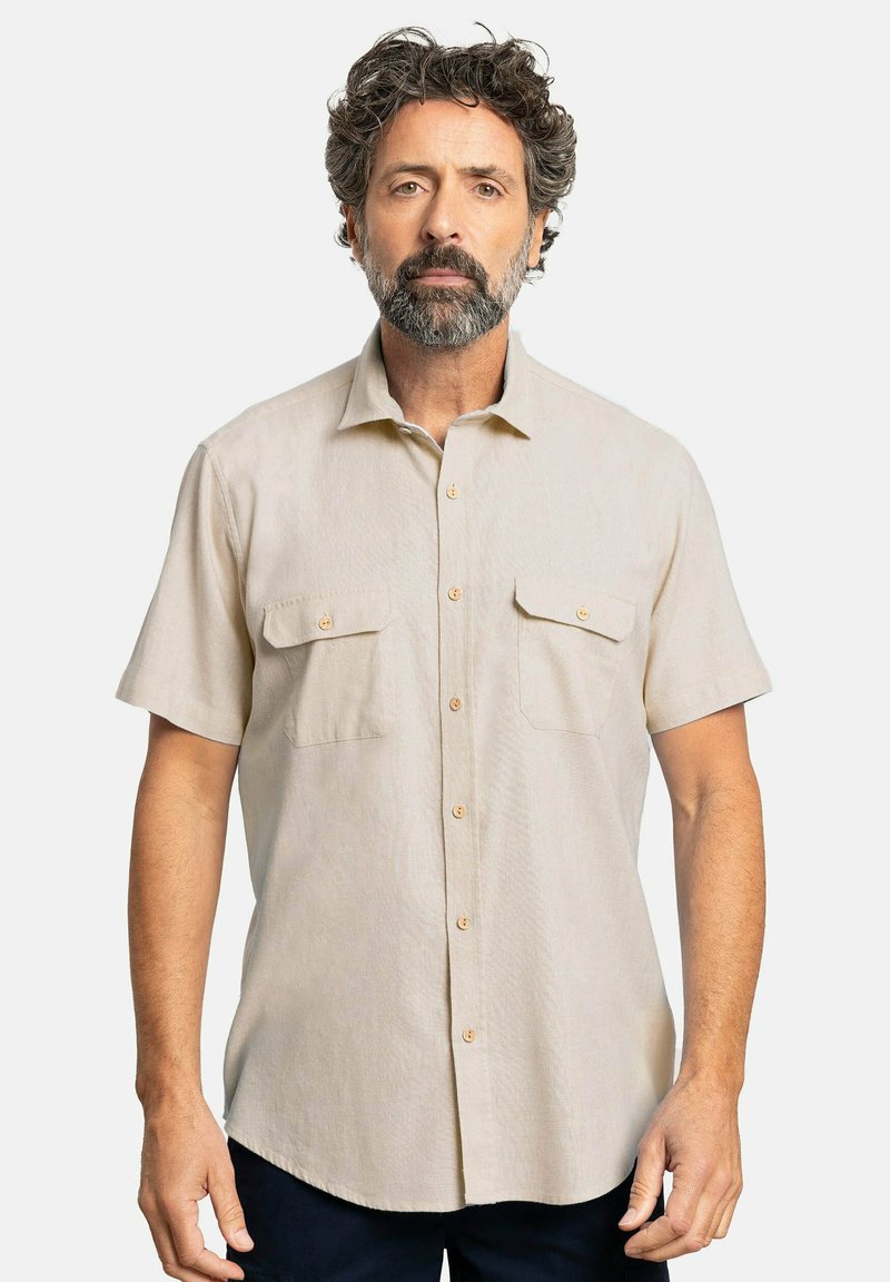 Camisa de manga corta color beige claro, con botones en la parte delantera, dos bolsillos en el pecho, textura suave y un sutil patrón horizontal. Diseño de cuello clásico.