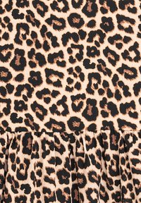 Leopardenmusterstoff mit schwarzen Flecken auf beigem Hintergrund, mit strukturierter Oberfläche und gekräuseltem Saum am unteren Rand.