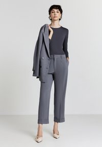 Completo grigio su misura con giacca attillata e pantaloni a gamba larga. Tessuto liscio, blazer doppiopetto, pantaloni con risvolto e scarpe flat beige.