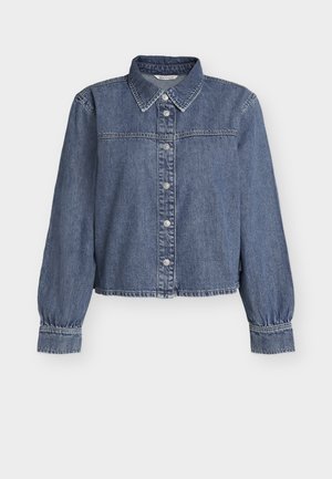 Kék farmerdzseki gombos elülső résszel, hosszú, felfújt ujjakkal, hegyes gallérral és összegyűrt mandzsettákkal.