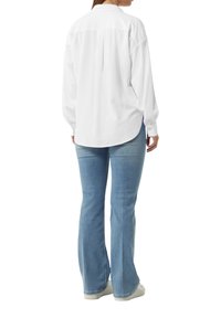 Witte langemouwen shirt met een subtiele gestreepte textuur, afgeronde zoom en met knopen sluitende manchetten, gecombineerd met lichtblauwe flared jeans en witte sneakers.